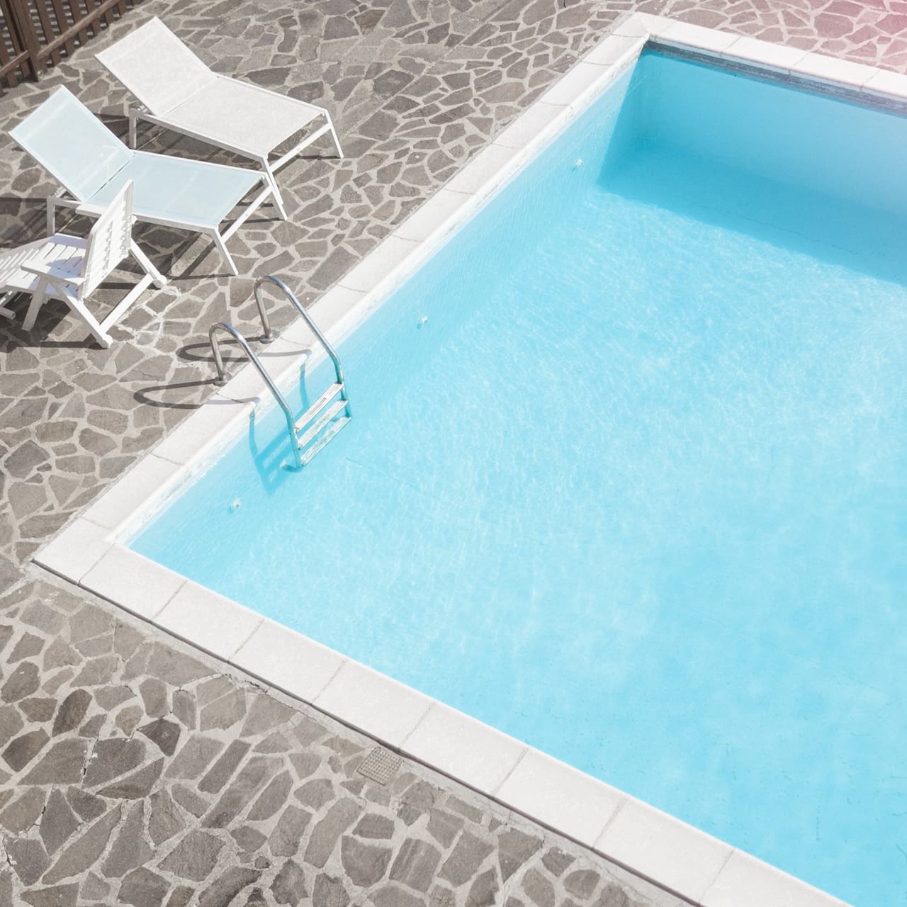 Rechteckiger Pool mit Steinplatten außenherum und drei Liegestühlen.