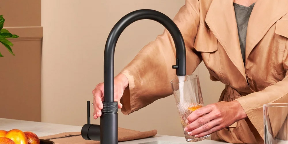 Person steht an Wasserhahn und befüllt ein Glas Wasser.