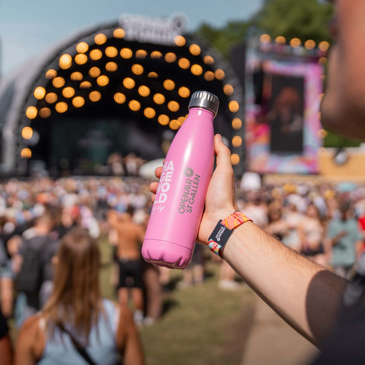 Mann hält Fläsche vor sich vor OpenAir-Bühne. 