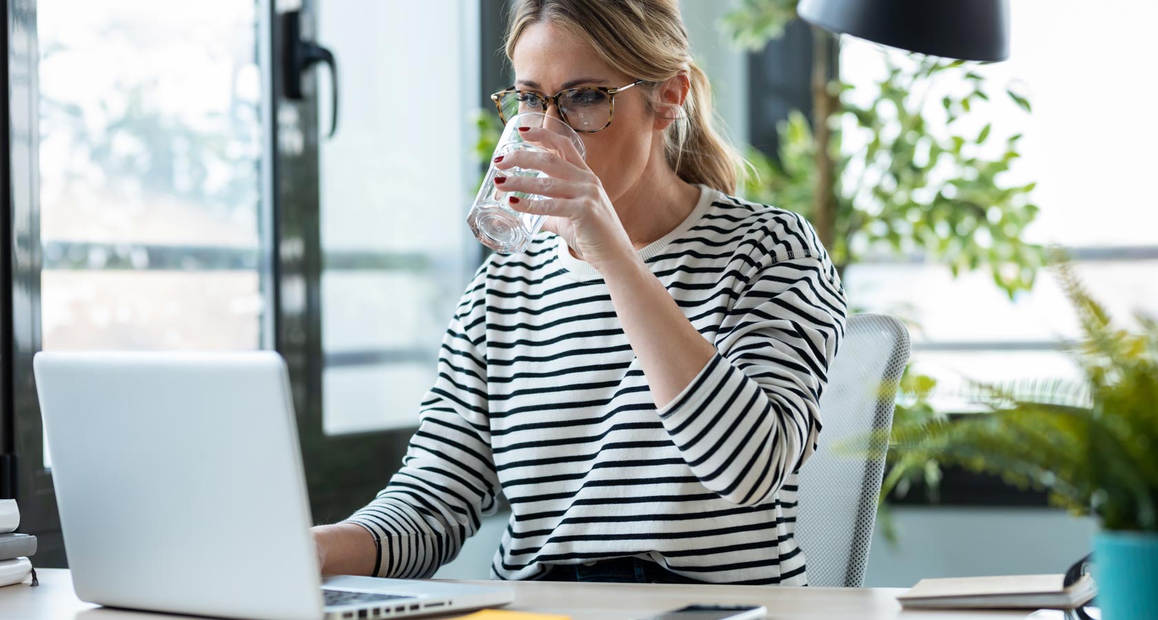 Eine Frau im Büro trinkt ein Glas Wasser von einem Wasserspender.