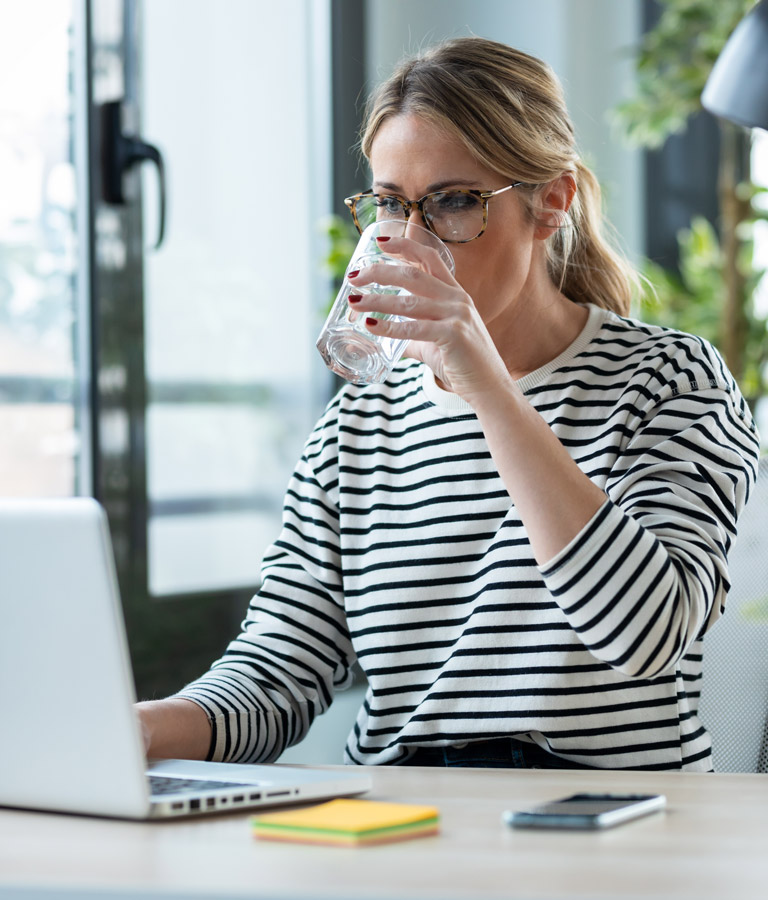 Eine Frau im Büro trinkt ein Glas Wasser von einem Wasserspender.