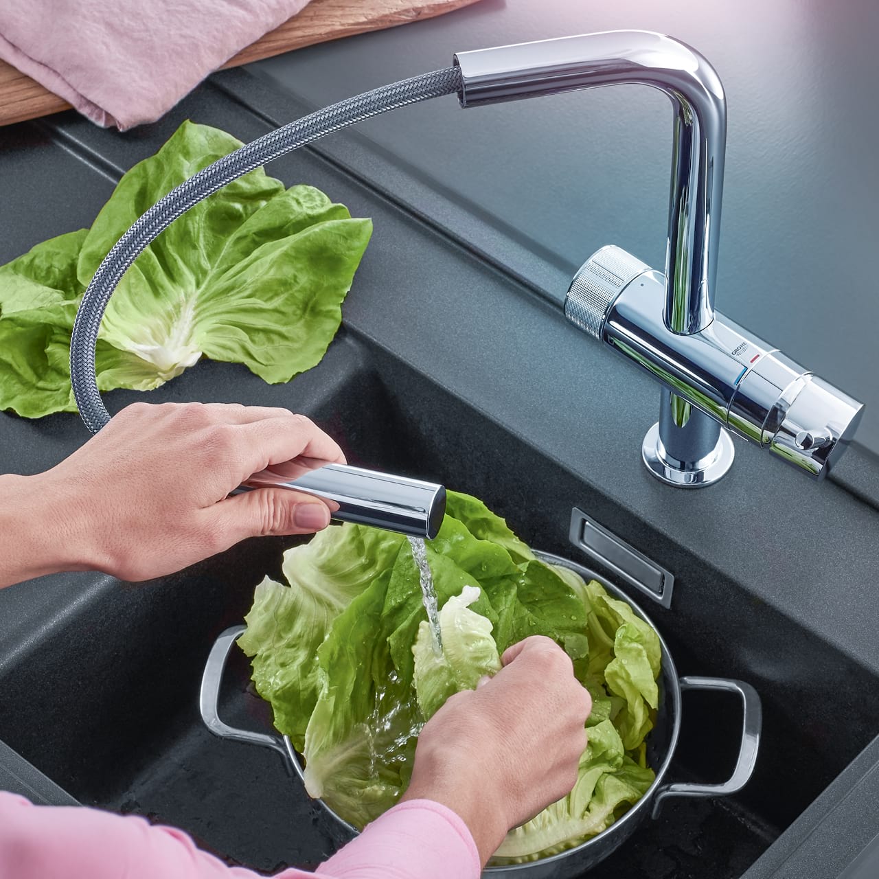 Hand hält ausziehbare Spülbrause der AQA drink Pure LOFT Küchenarmatur und wäscht Salat.