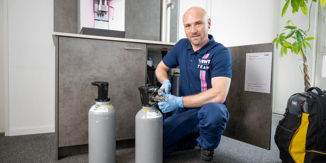 Mann macht gerade Service an einem Wasserspender.