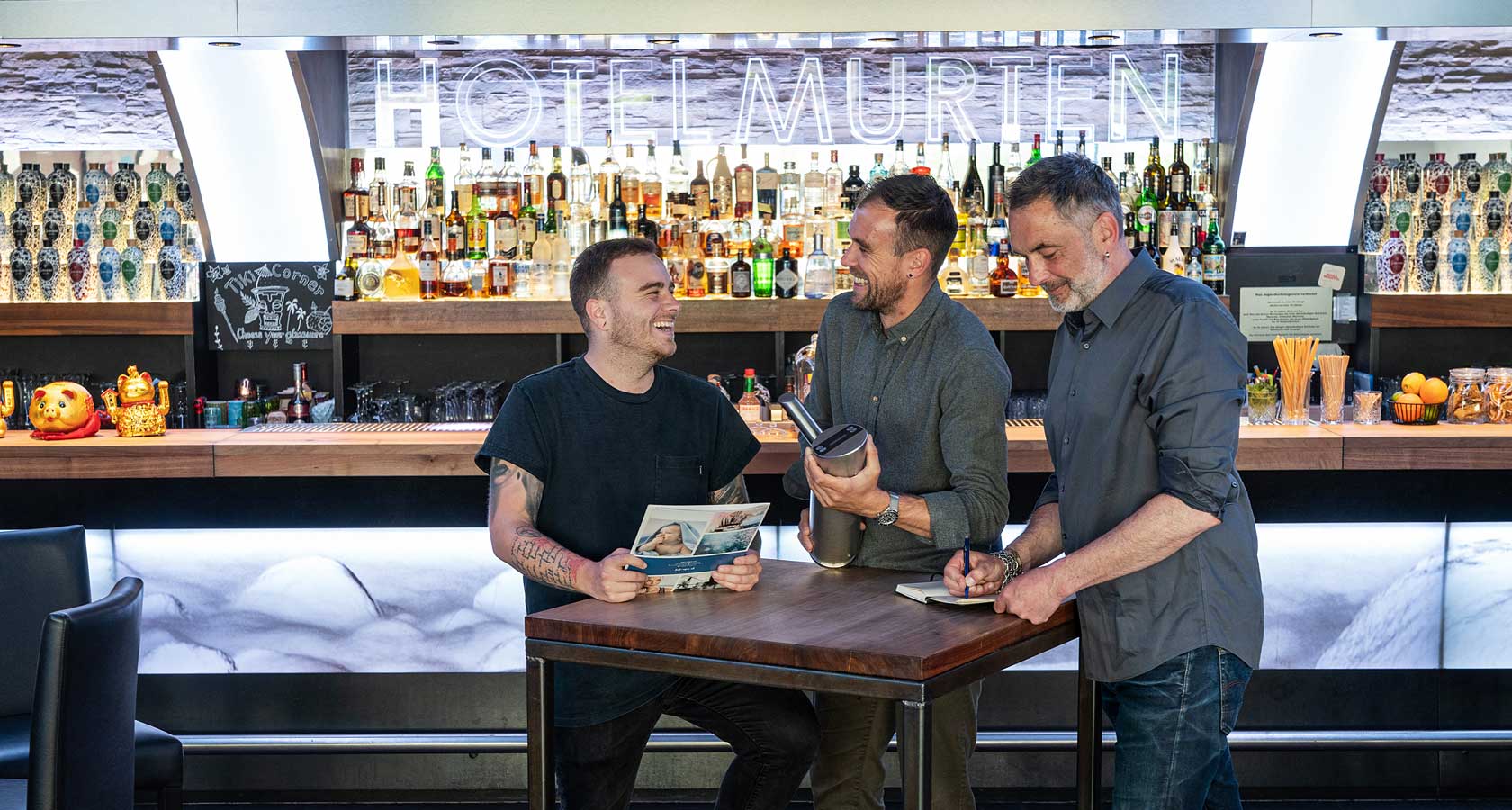 Trois hommes se tiennent à une table de bar.