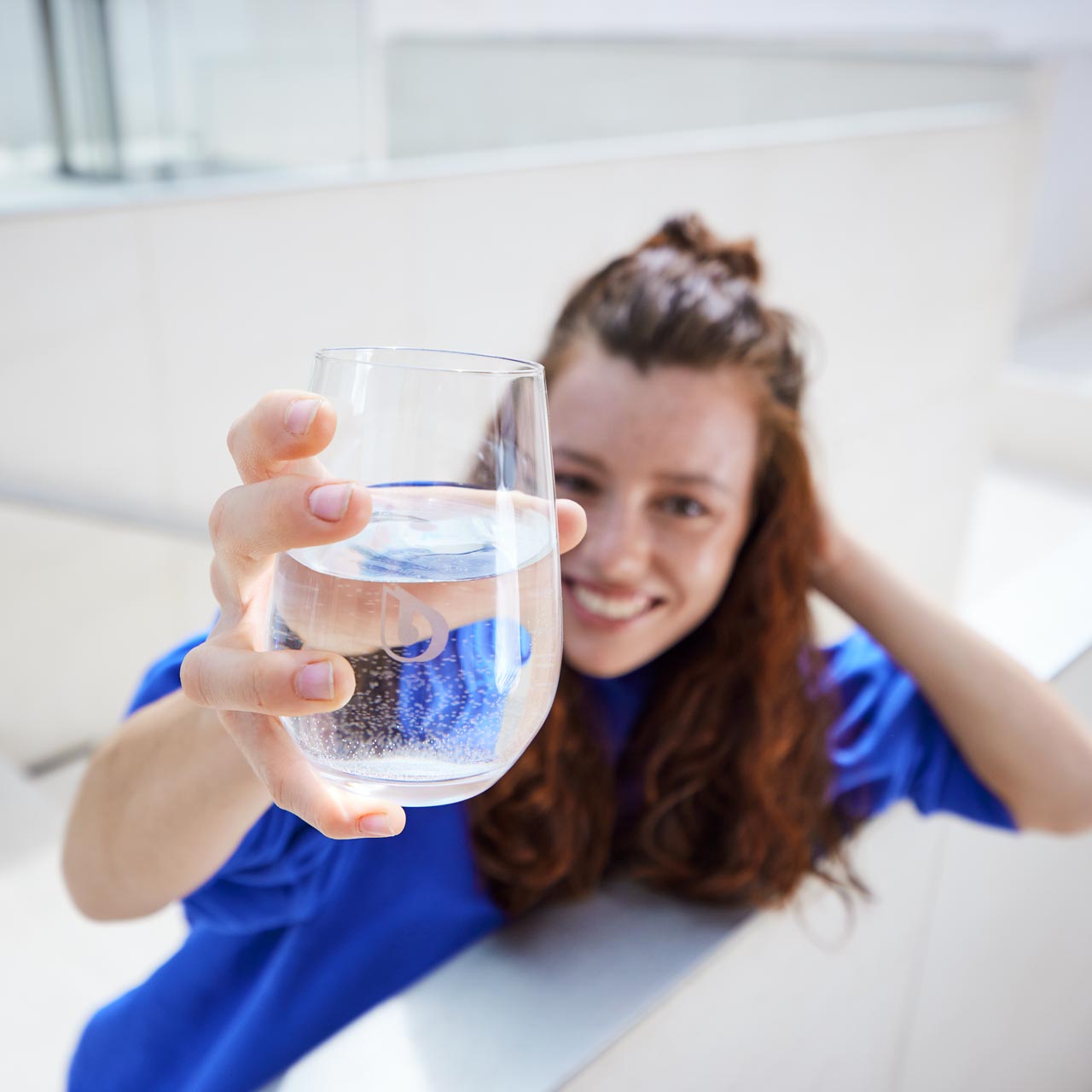 Une femme tend un verre d'eau en direction de la caméra. 
