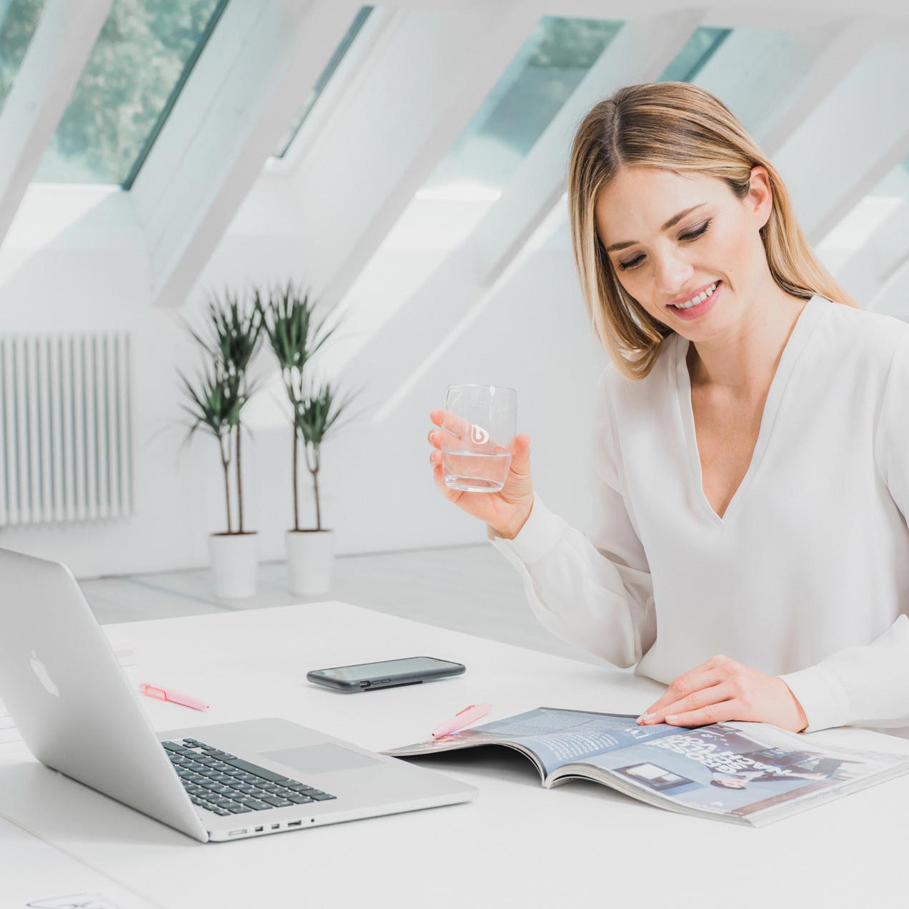 Une femme est assise à une table de bureau et tient un verre d'eau.