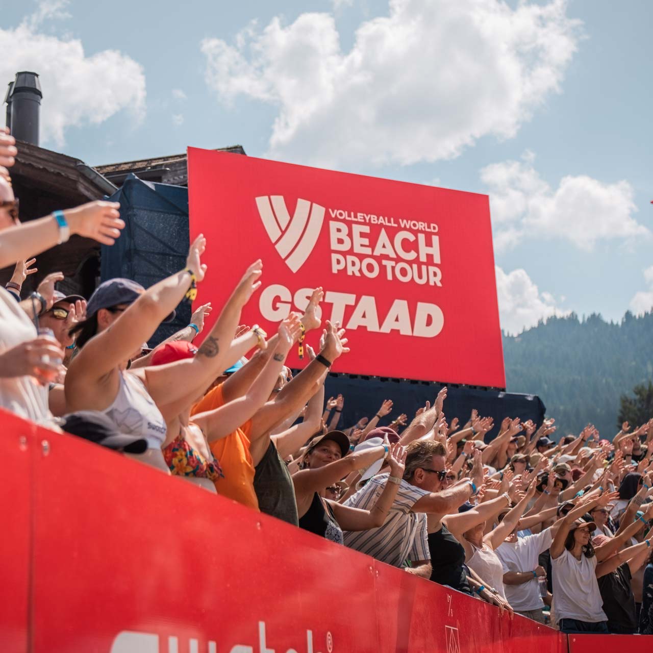Le public tient les mains en l'air dans le stade, devant un écran rouge.