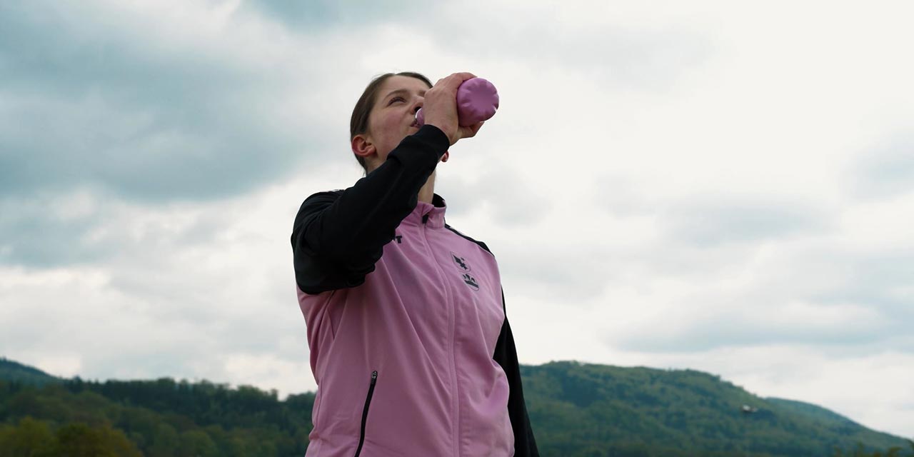 Une femme boit dans une fausse bouteille, avec des montagnes en arrière-plan.