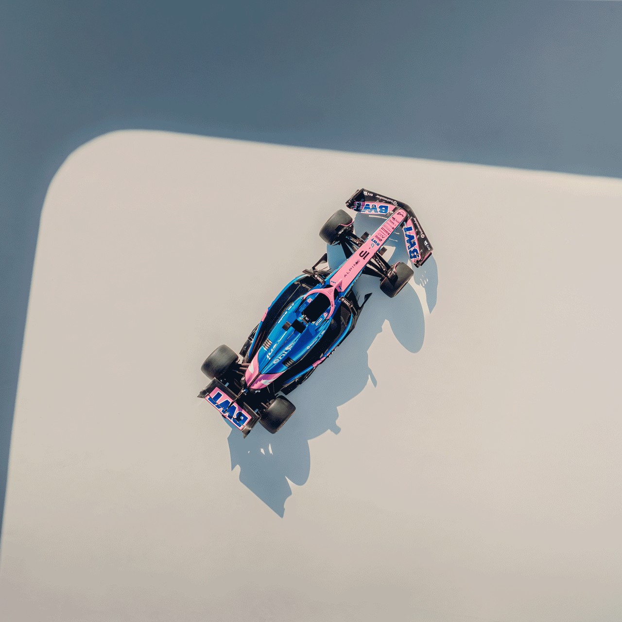 Une voiture de Formule 1 aux couleurs bleu et rose, photographiée d'en haut.